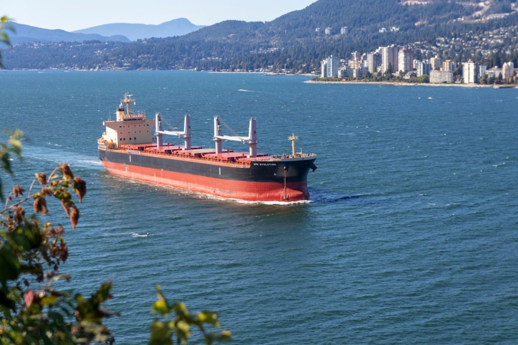 cargo-ship-sailing-near-city-bmpjcuc9dv8